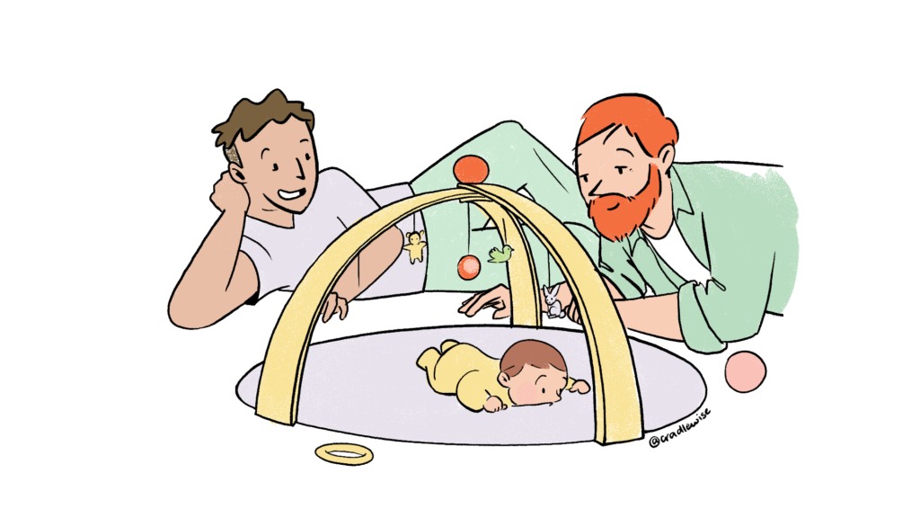 Two dads playing with their baby lying on the playmat